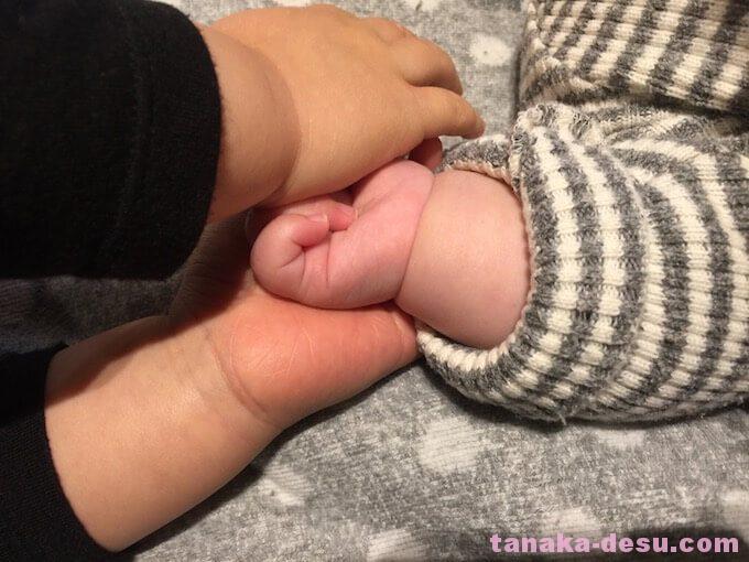 4ヶ月の妹の手を握る1歳児